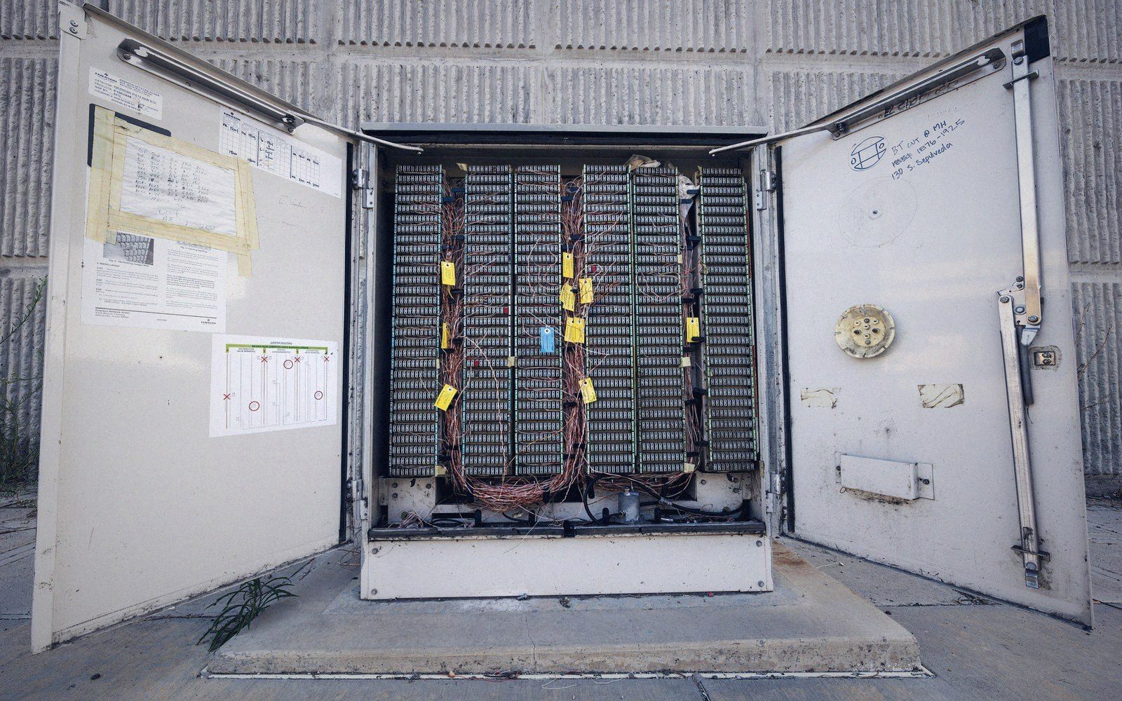 Open equipment cabinet reveals rows of wired copper telecom cable connections and terminals