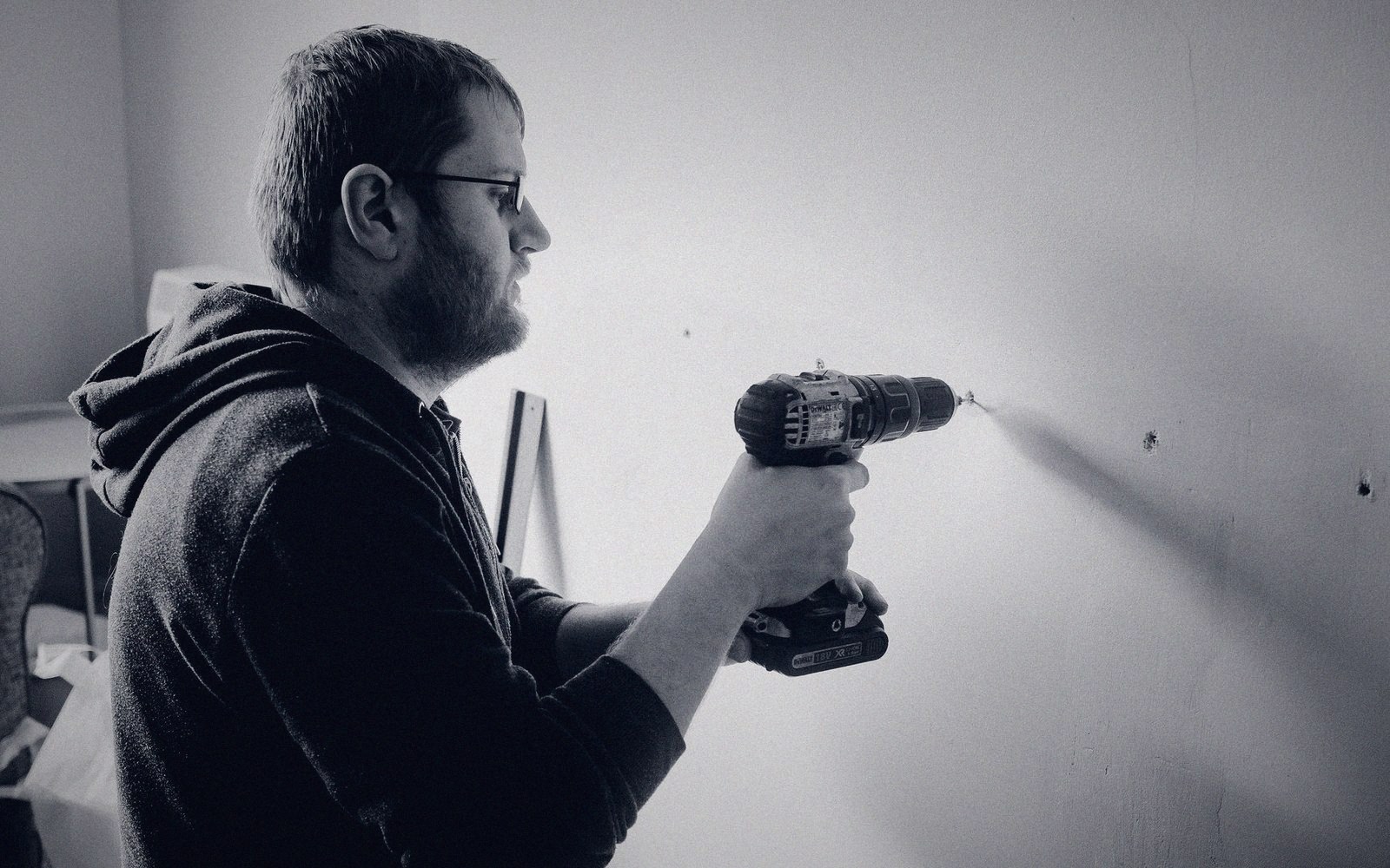 Man using a cordless power drill to bore a hole into an interior wall