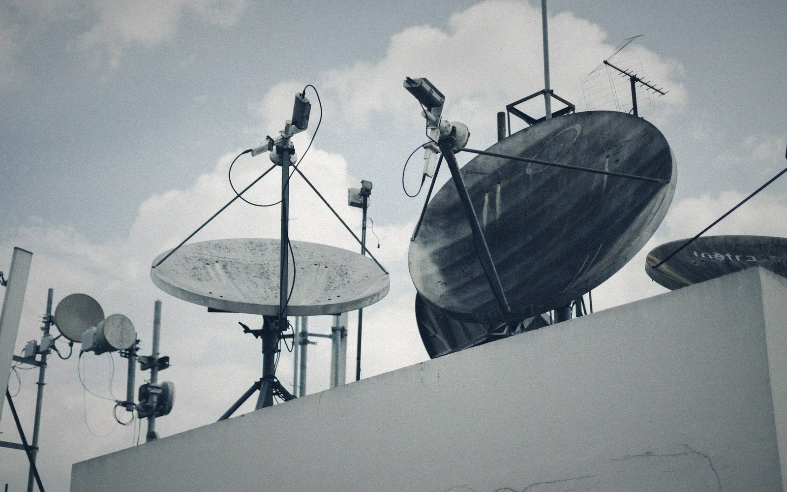 Satellite dishes and antennas cluster on a rooftop against a cloudy sky