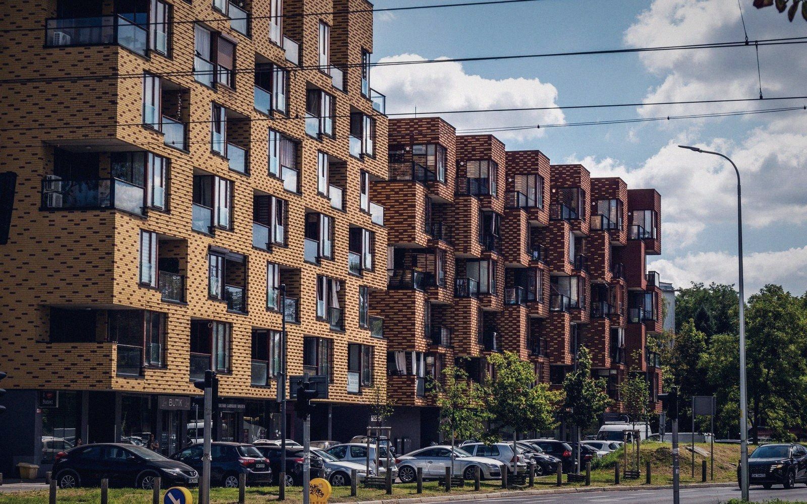 Apartment buildings with patterned brick facades and projecting box balconies above a parking lot