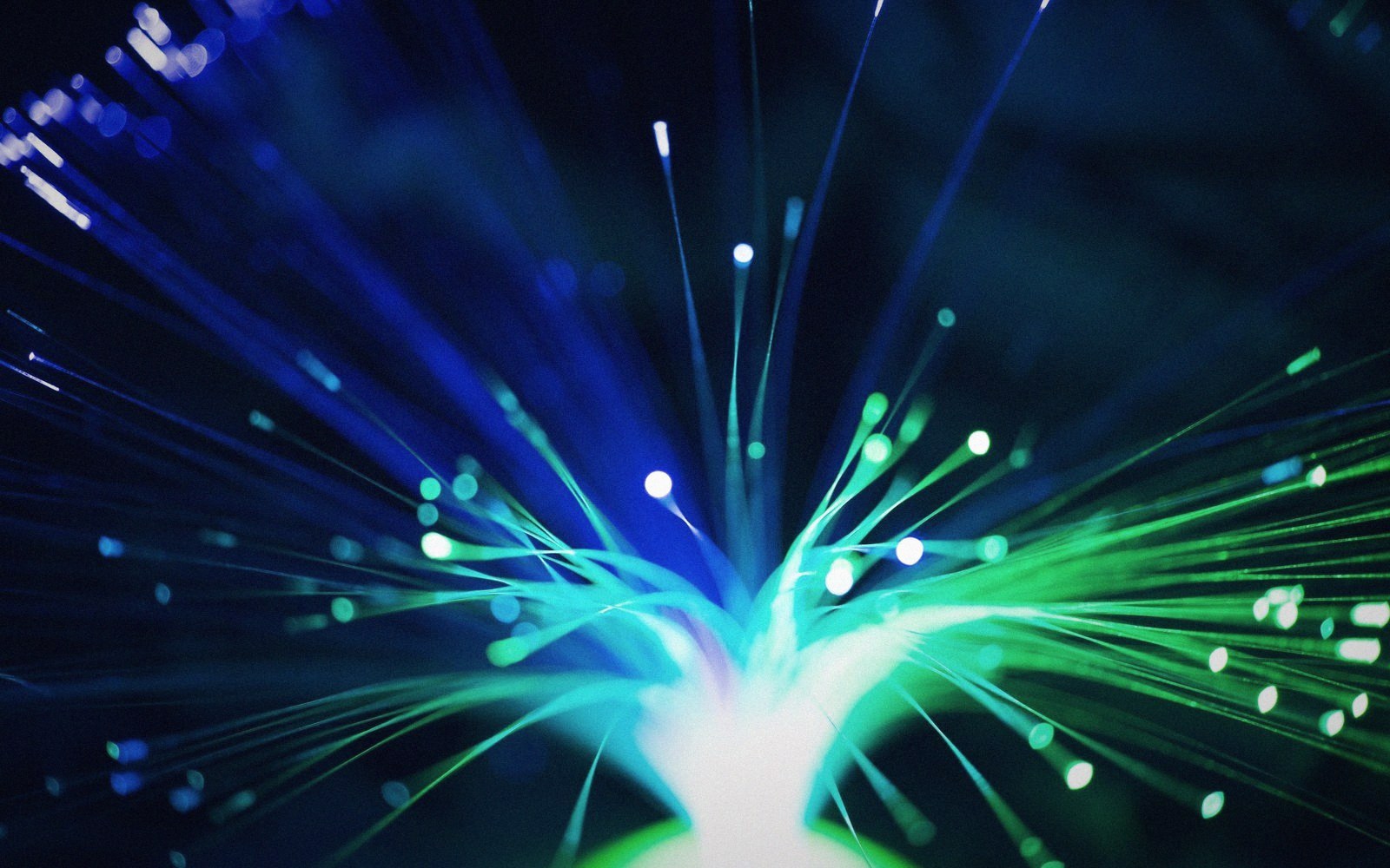 Fibre optic strands glow blue and green as light bursts outward from a central point