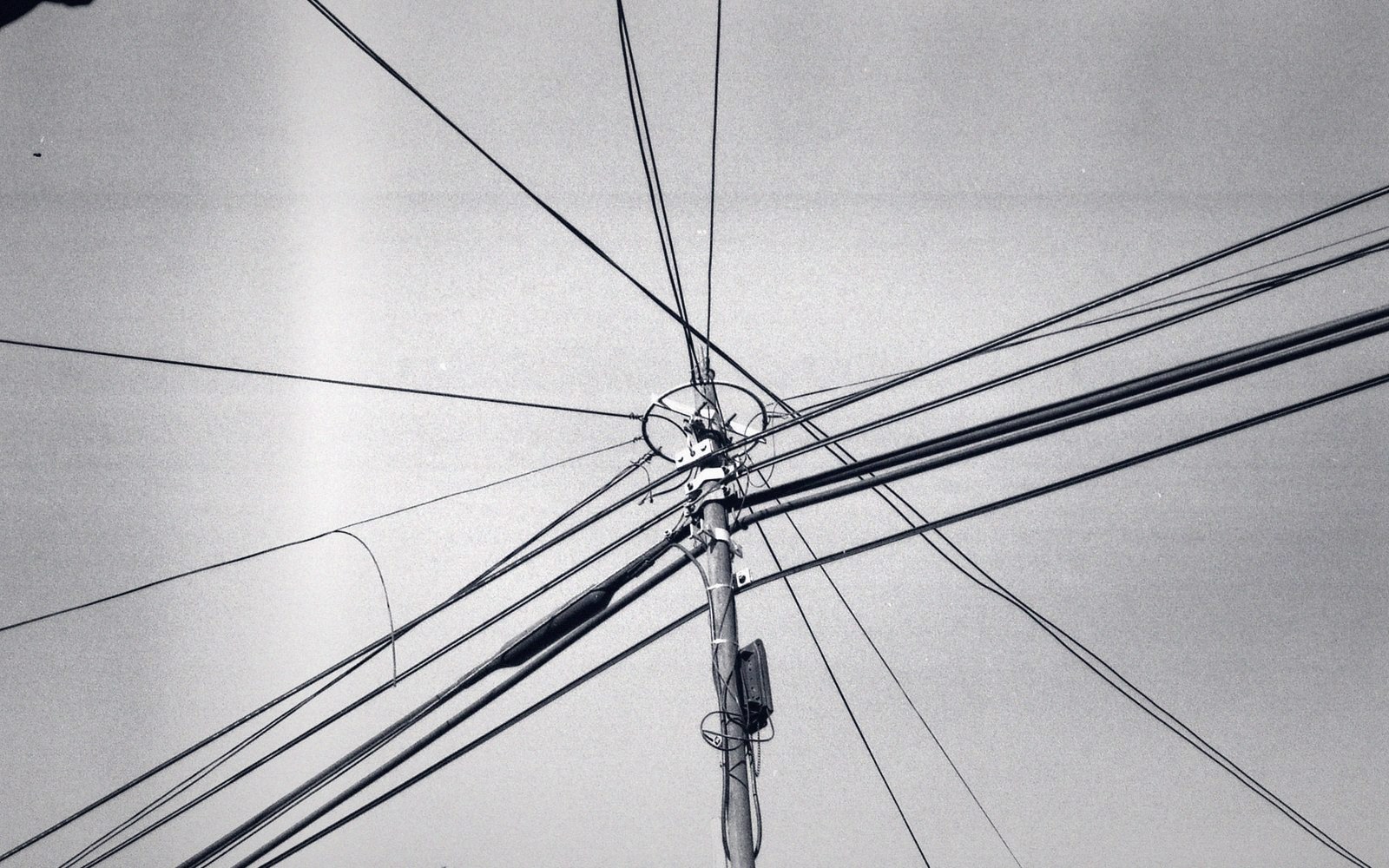 Utility pole with numerous overhead wires crossing at odd angles against the sky