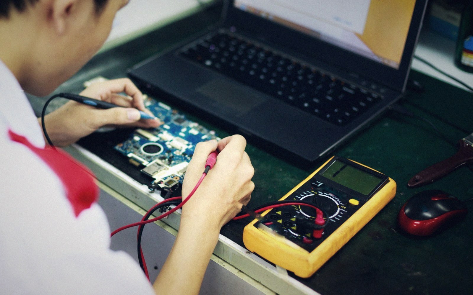 Technician uses a multimeter to test a laptop motherboard removed from its case