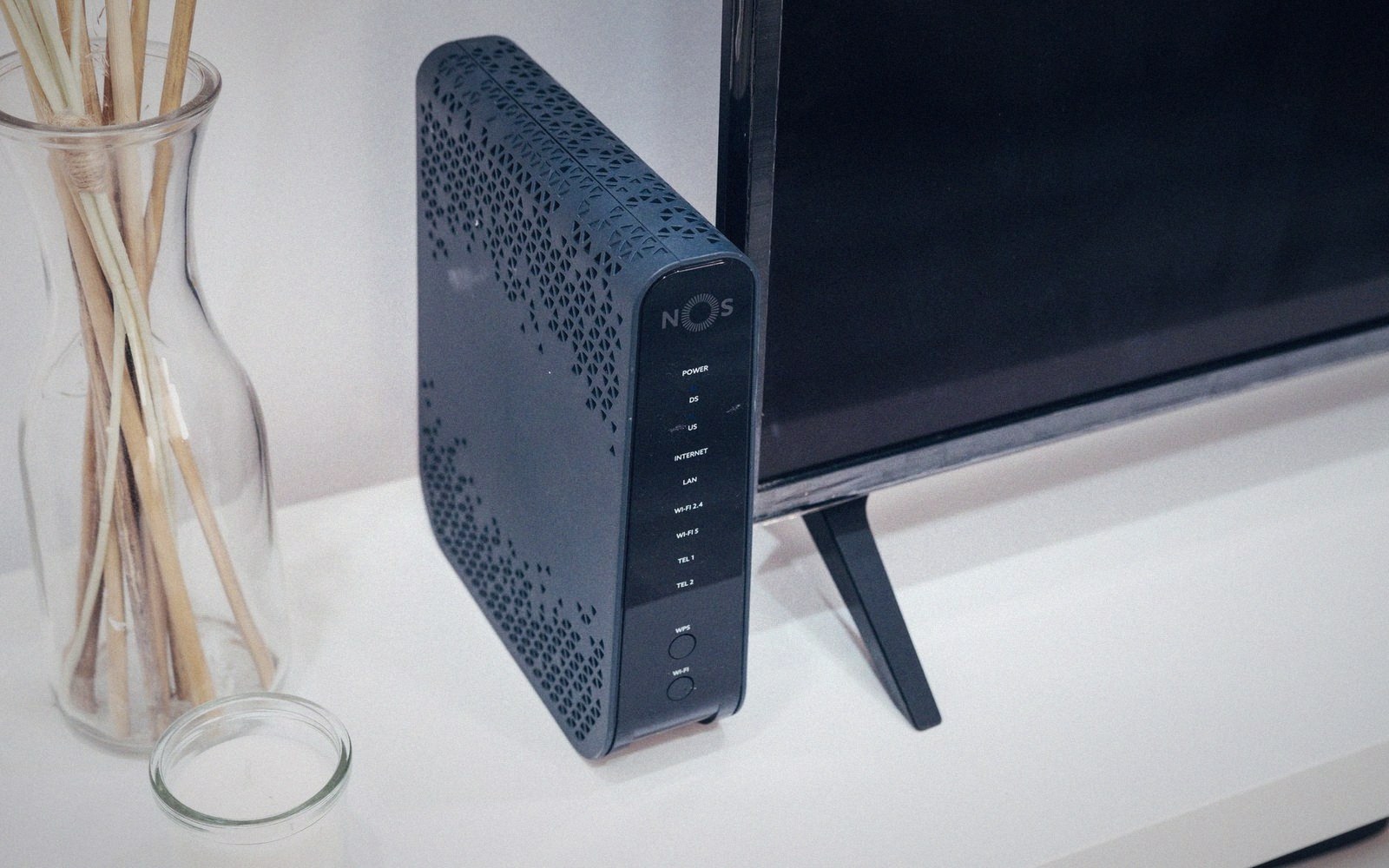 A NOS router placed upright on a shelf beside a television screen