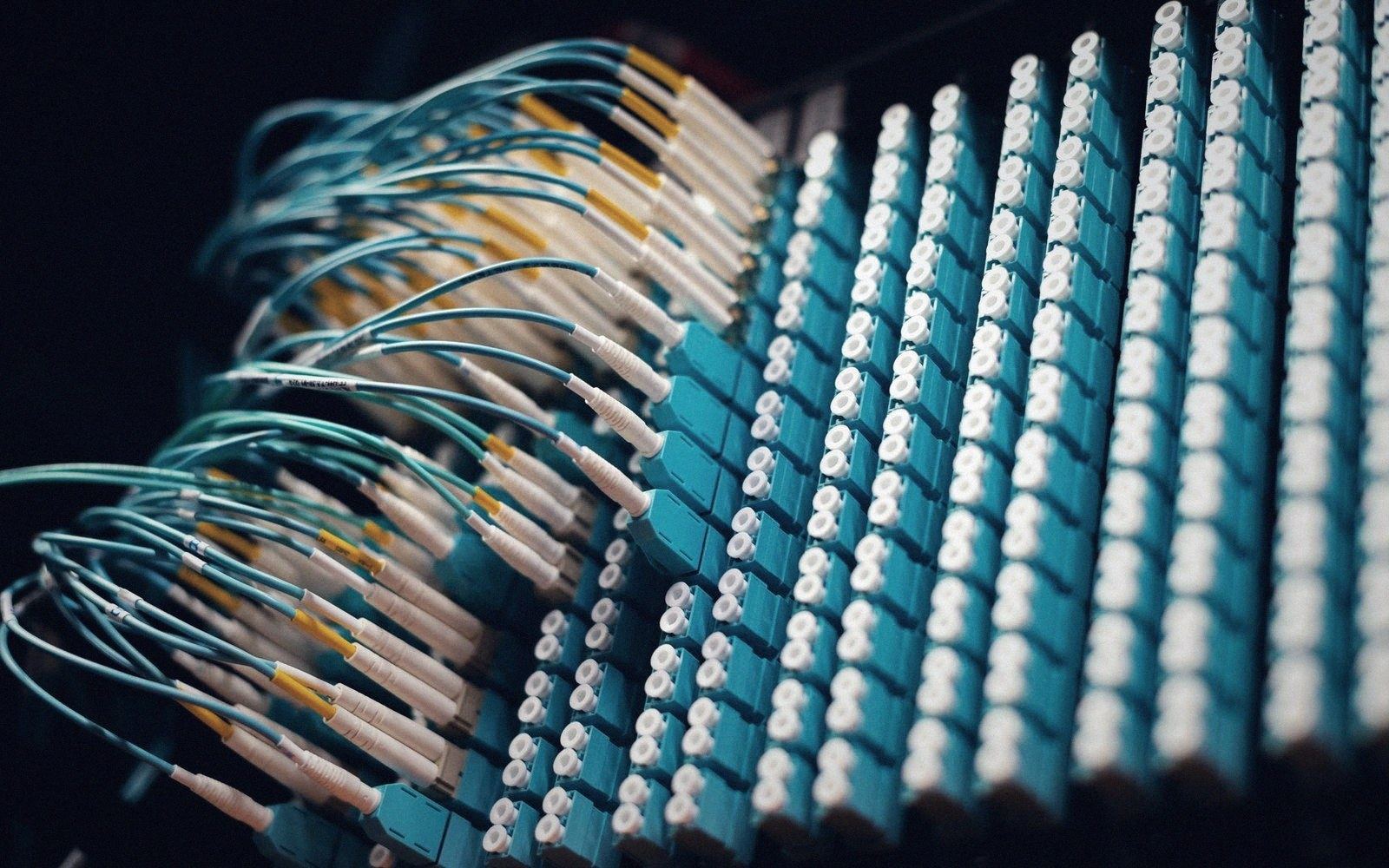 Fiber optic cables plugged into rows of teal patch panel ports