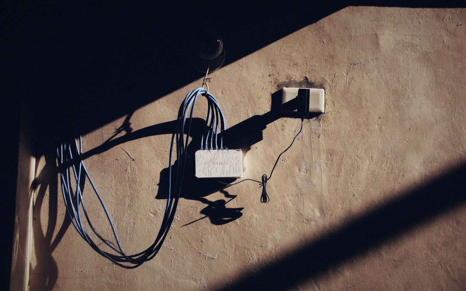 Coiled network cable hangs beside a small router mounted on a sunlit wall